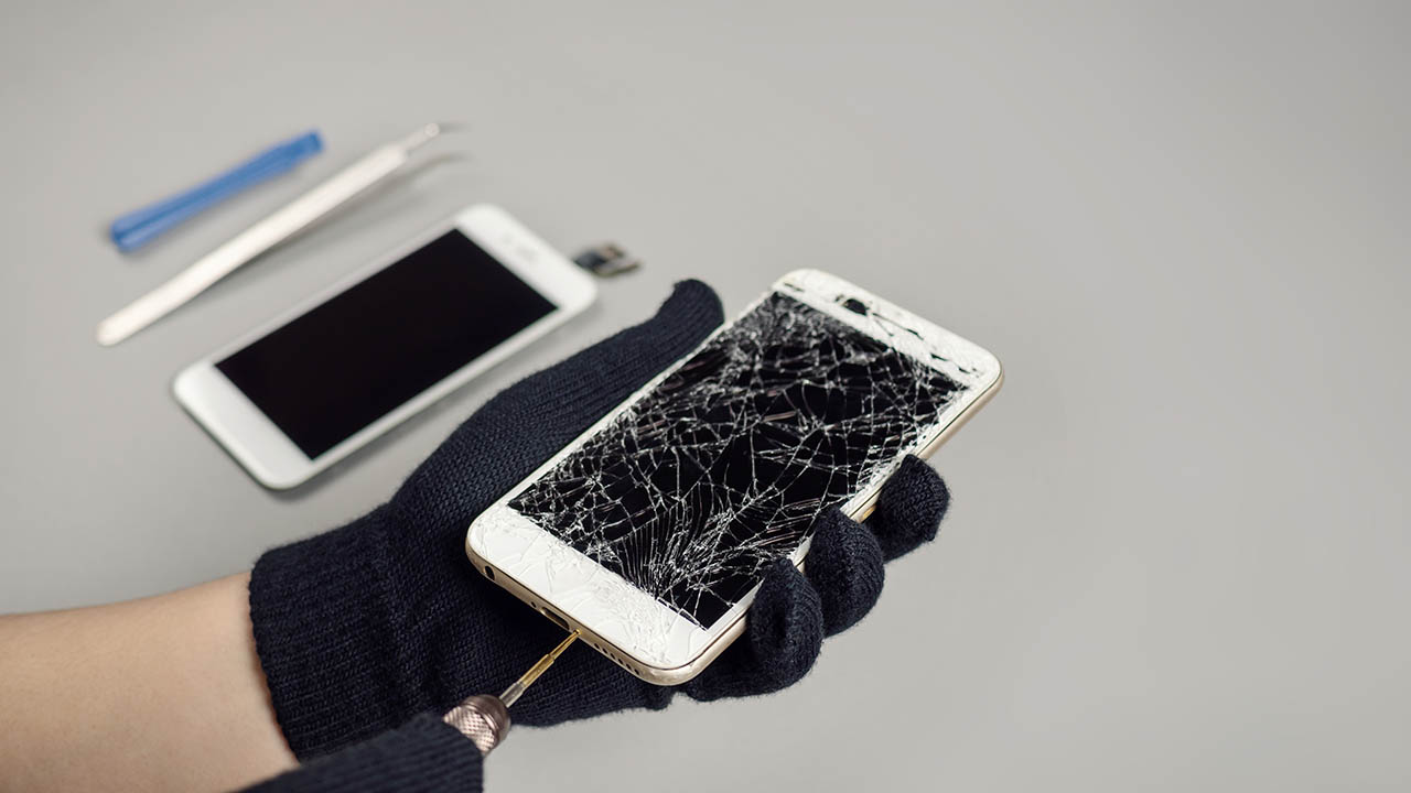 修理用の工具と画面が割れたスマートフォンを点検する様子