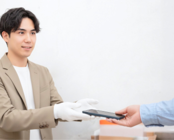 梱包材の並ぶカウンターで、手袋をしたスタッフがお客様からスマートフォンを受け取る様子