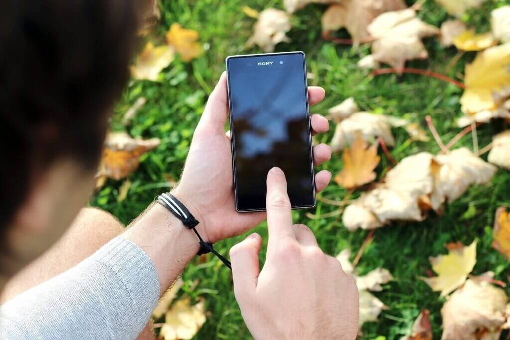 屋外で黒いXperiaを手に持ち、売却前に画面を操作して中身を確かめている様子